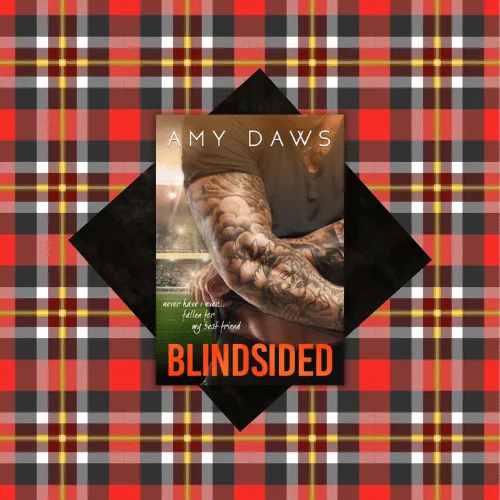 Alt Text Description: The image features the book cover of "Blindsided: A Best Friends to Lovers Standalone" by Amy Daws. The cover shows a close-up of a tattooed man’s arm, with the title "BLINDSIDED" in bold orange letters at the bottom and the author’s name, "AMY DAWS," at the top. The background is a red, black, yellow, and white plaid pattern with a black diamond shape framing the book cover. The image supplements a book review. Book Title: Blindsided. Author: Amy Daws.